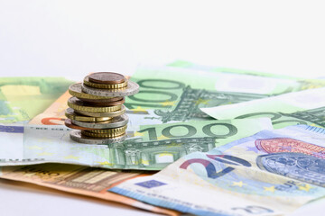 Tower with euro coins over euro banknotes on white background.