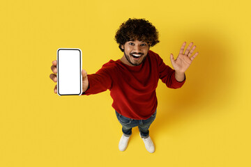High angle view of indian guy showing smartphone, mockup