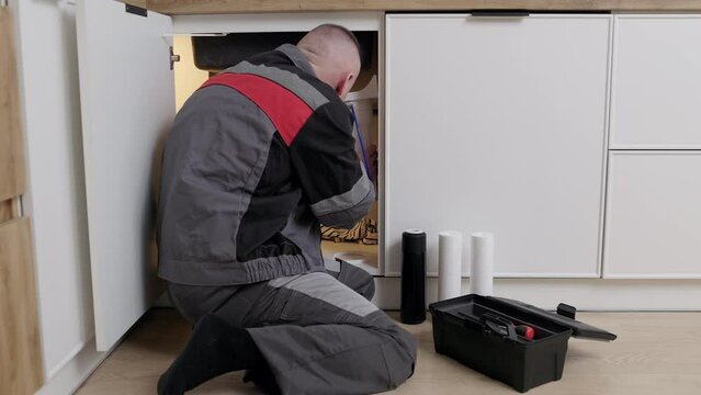 Repairman in overalls installs or changes drinking water filters under the sink in the kitchen. Service concept household filtration system. Timely replacement of water cartridges is healthy life