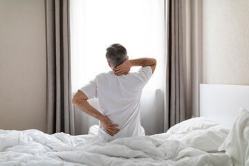 Unrecognizable grey-haired man sittting on bed, touching back and neck