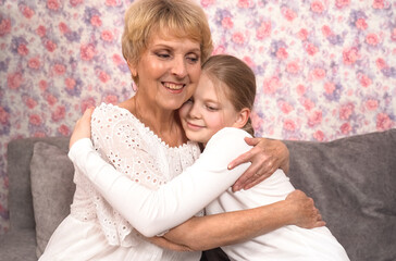 A loving elderly grandmother hugs and kisses her teenage granddaughter.