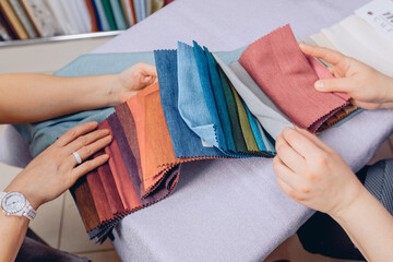 The hands of the seller and the buyer sort through the various pieces of fabric to select the right...