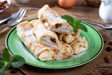 Pancakes stuffed with cottage cheese and raisins on wooden table. A delicious sweet dessert