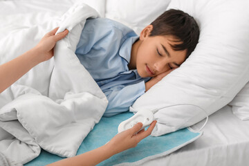 Woman turning on electric heating pad for her little son in bedroom © Pixel-Shot