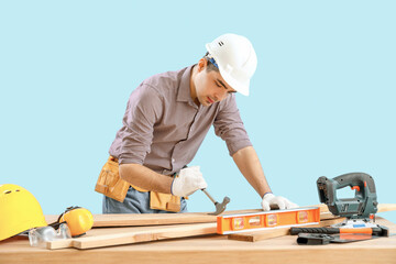 Young carpenter with hammer and wooden planks at table on blue background