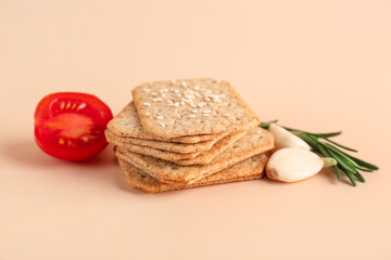 Fototapeta na wymiar Stack of tasty crackers with sesame, garlic, tomato and rosemary on beige background