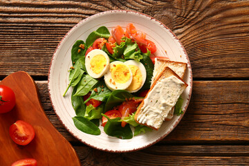 Plate of delicious salad with boiled eggs and salmon on brown wooden background