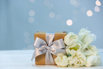 Gift and beautiful tulip flowers for Mother's Day celebration on light wooden table against blurred lights