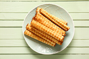 Plate of wafer rolls with boiled condensed milk on green wooden background