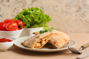 Plate with baked meat empanadas, sauce, tomatoes and lettuce on color table, closeup