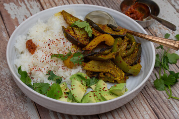 Spicy eggplant, bell pepper and rice, avocao in thite bowl on wooden table
