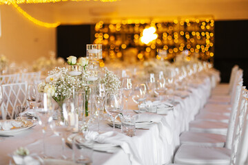 Served wedding table with decorative fresh white flowers and candles. Celebration details. Hanging flower beds and light bulbs Wedding decoration and decor, floristic concept