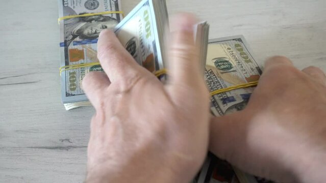 4K view of male hands taking a bunch of stacks of dollar bills.