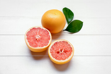 Composition with ripe grapefruits and plant leaves on light wooden background