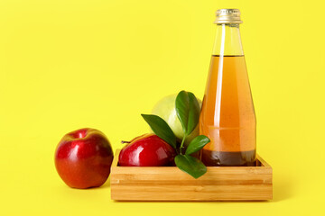 Glass bottle of fresh apple cider vinegar and fruits on yellow background
