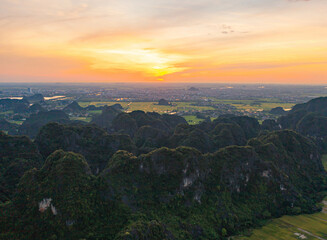 Fototapeta premium Aerial top view of fresh paddy rice, green agricultural fields with mountain hills valley in countryside or rural area of Ninh Binh, in Asia, Vietnam. Nature landscape background.