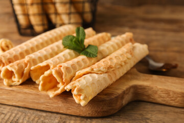 Board with delicious wafer rolls and mint on wooden background