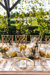 Wedding decorations. Served wedding table with golden plates, napkins, decorative fresh and dried flowers, candles and and light bulbs. Celebration details, wedding outdoor	

