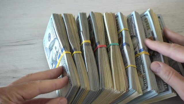 4K view of hands counting bundles of dollar bills tied with rubber bands.