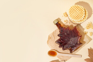 Waffles, bottle and spoon of tasty maple syrup on beige background