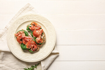 Plate of tasty bruschettas with ham on white wooden background