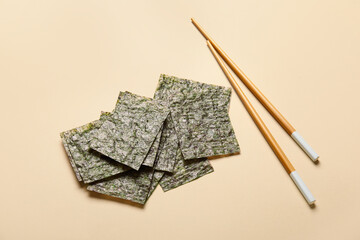 Nori sheets and chopsticks on color background