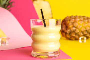 Glass of tasty pineapple smoothie, straw and ice cubes on colorful background