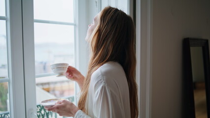 Satisfied lady enjoying cup of coffee at home closeup. Woman watching window