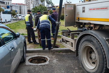 Sewer workers cleaning manhole and unblocking sewers the street sidewalk