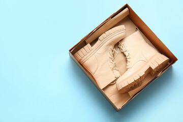 Cardboard box with stylish shoes on light blue background