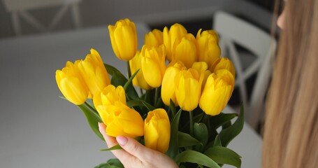 Back shot of anonymous woman touch yellow tulip bunch and enjoy beauty. Beautiful spring bouquet with rich foliage at home.