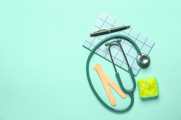 Stethoscope, notebook and pills on turquoise background