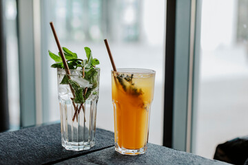 Water with green mint leaves and orange juice in a glass on a restaurant table 