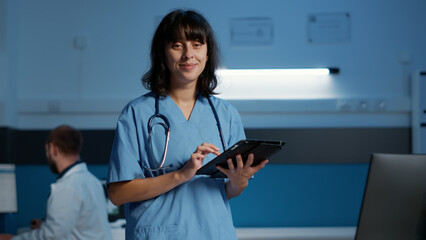 Portrait of serious nurse working night shift in hospital office while typing medical expertise on computer. Physician assistant planning medication treatment to help cure patient disease.