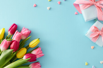 Flat lay photo of present boxes bouquet of flowers yellow pink tulips colorful hearts baubles on isolated pastel blue background with empty space in the middle. Happy Mother's Day concept