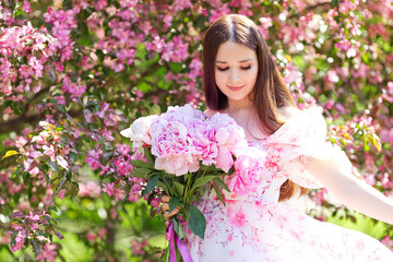 Fototapeta premium A girl dancing with a bouquet of pink peonies in a blooming garden