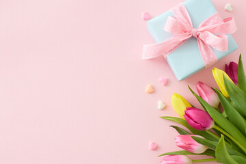 Flat lay photo of giftbox bouquet of flowers yellow pink tulips colorful hearts on isolated pastel pink background with empty space. Happy Mother's Day idea