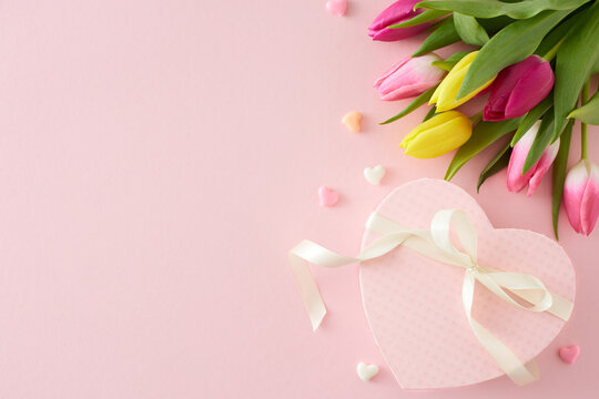 Top view photo of heart shaped gift box with bow colorful tulips flowers hearts baubles on isolated pastel pink background with copyspace. Happy Mother's Day concept