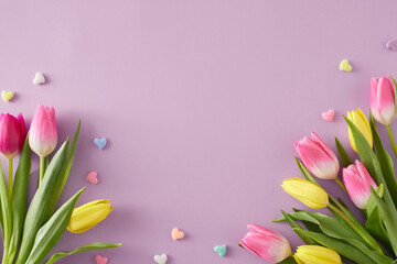 Mother's Day atmosphere idea. Top view composition of bouquets of pink yellow tulips flowers and colorful hearts baubles on isolated light violet background with copyspace