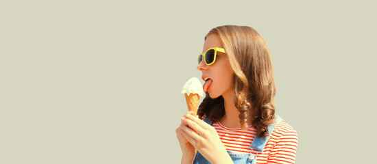 Portrait of happy young woman eating ice cream wearing summer sunglasses on gray background