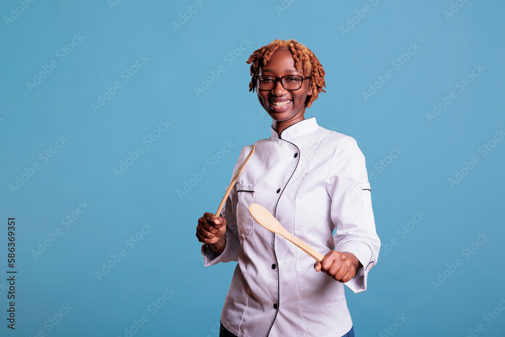 Wall mural optimistic kitchen professional playing with wooden kitchen utensils in studio shot. female chef in 