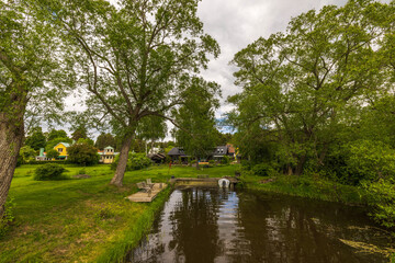 Fototapeta premium Beautiful view of village pond coast with outdoor furniture for residents. Sweden. Europe. 