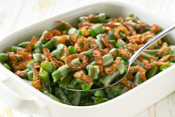 close up green bean casserole with crispy fried shallots and cream sauce in a ceramic cooking baking dish.