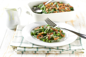 Homemade roasted green bean casserole with crispy fried shallots in a ceramic bowl on a white wooden table, close up.