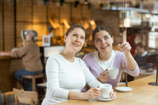 Two cheerful women chatting and drinking coffee at the bar counter of a cafe