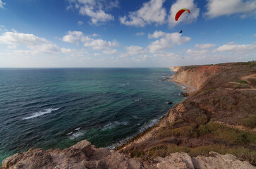 Rocky Israel seashore top view. A man is flying in the air on a paraglider