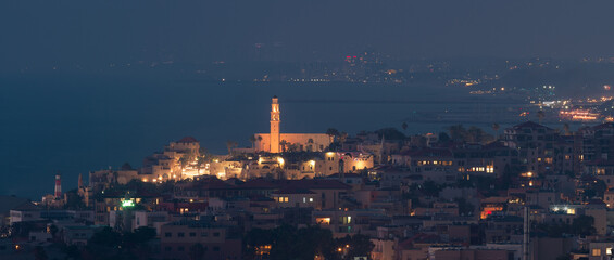 Jaffa city night panorama. St. Peter's Church tower and Tel Aviv on the background