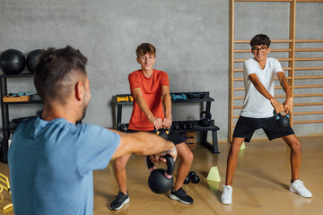 Unrecognizable trainer instructor shows lifting exercise with dumbbell weight in a big gym,...