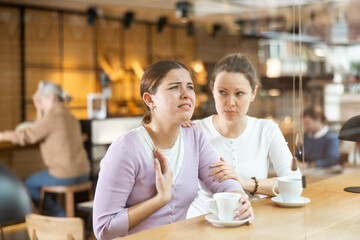 Caring empathetic woman comforting upset younger sister while sitting together at cozy cafe over cup of coffee