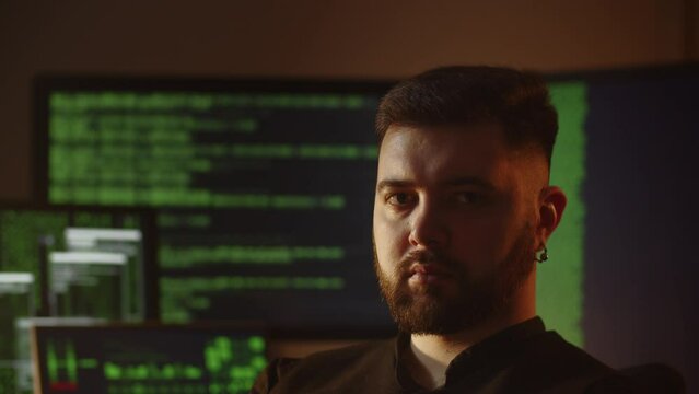 Bearded programmer posing with computer screens on the background. Hacker is breaking the code. Software developer is coding in the office. Internet security
